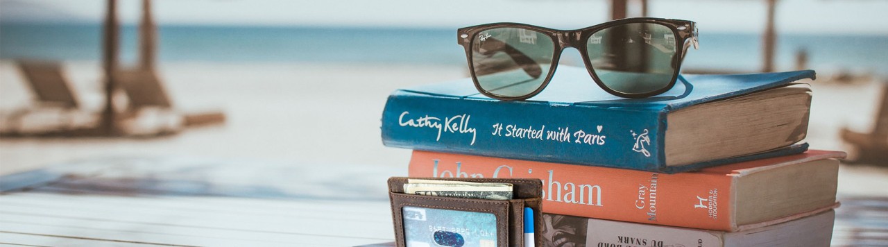 Urlaub am Strand mit Bücherstapel und Sonnenbrille und Geldbeutel mit Kreditkarte